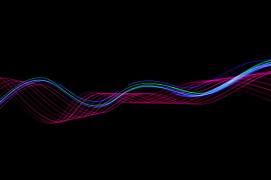 Long exposure photograph of neon pink and blue colour in an abstract swirl, parallel lines pattern against a black background. Light painting photography.