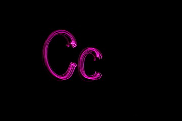 Long exposure photograph of the letter c in pink neon color, in upper case and lower case, parallel lines pattern against a black background. Light painting photography.