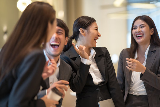 Asian business people talking and laughing in office building. Young businessman and businesswoman colleague talk to each other during the break.