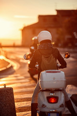 Travels by scooter. girl riding motor scooter on road at sunset.