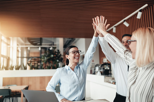 Laughing businesspeople high fiving together in an office