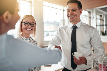Smiling businesspeople shaking hands together over coffee