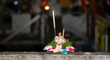 A krathong with candles placed on a metal rail and is about to be released into the river.