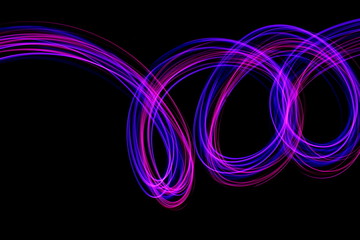 Long exposure photograph of neon pink and purple colour in an abstract swirl, parallel lines pattern against a black background. Light painting photography.
