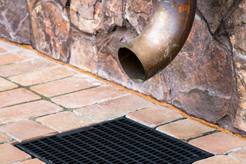 Gutter downspout on the wall of house. Metal rain downspout at home exterior. Spout of gutter pipe and grille of drainage system closeup.