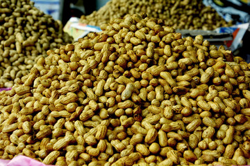 Heap of unpeeled, dried and roasted golden groundnuts, peanuts also known as goober or monkey nuts with shells classified as Arachis hypogaea being sold by vendor 
