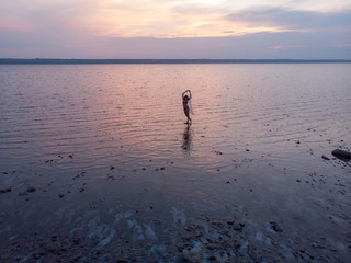 Silhouette of a girl in the middle of lake at sunset. Beautiful girl posing alone in shallow water with light ripples