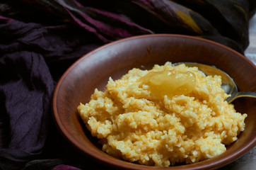 Porridge with rice and pumpkin with a spoon of honey in a clay plate with a hug of dark fabric