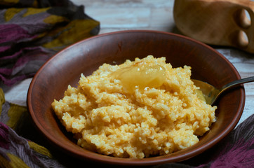 Porridge with rice and pumpkin with a spoon of honey in a clay plate and wooden peel with a hug of dark fabric