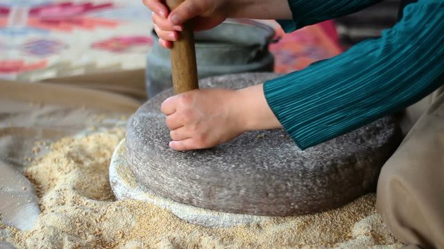 Woman is grinding wheat by hand in stone mill