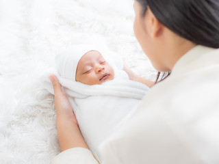 A beautiful Asian woman is looking at her newborn baby with happiness and love