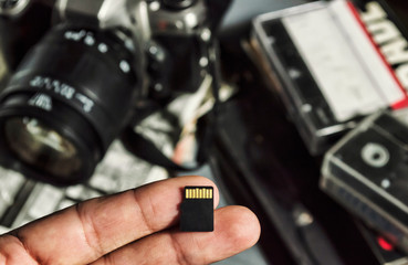 Micro sd card lies on your fingers. Retro camera, old photos and video tapes on background. Flash...