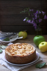 Pie with apple cream filling, apples and dishes on a wooden background. Rustic style.