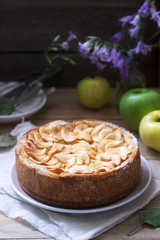 Pie with apple cream filling, apples and dishes on a wooden background. Rustic style.
