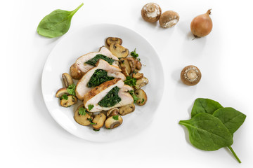 chicken breast fillet with spinach filling, mushrooms, onion and parsley garnish on a plate, some raw ingredients dispersed on the white background, copy space, high angle view from above