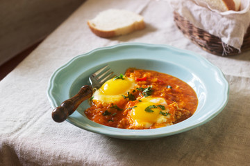 Shakshuka with bread on a wooden table. Middle eastern traditional dish. Homemade. Selective focus.