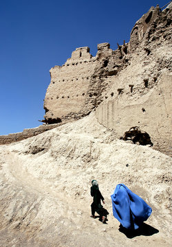 A girl and woman walk over the wall of Ghazni citadel in Ghazni, Afghanistan. The woman wears a blue burqa (burka), traditional in central Afghanistan. Afghan women in burqa (burka) local clothes.