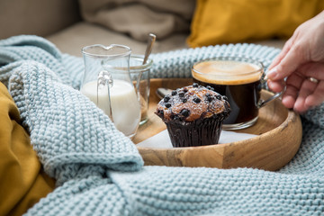 Frau trinkt Kaffee mit Blaubeermuffin, Milch und Zucker auf Holztablett und gemütliches Sofa mit...