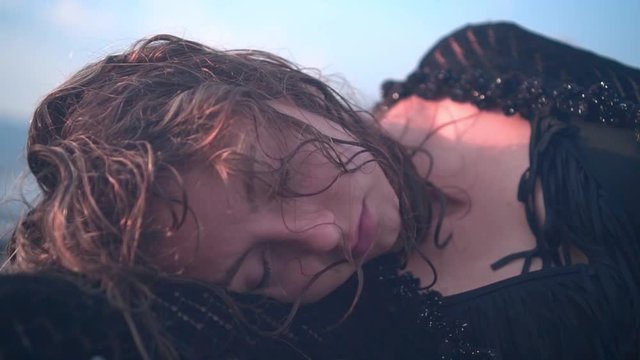 A young girl lying on the seashore unconscious, without movement. A woman lies face down on the shore with wet hair and clothes. Close-up.