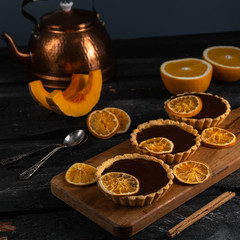 chocolate orange tartlets on a wooden board, dark background, cinnamon stick, dessert