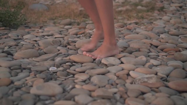 Close-up. Female tanned legs barefoot walk on the rocky seashore, the girl is uncertain, stumbling.