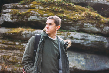 Portrait of young man in khaki parka jacket with backpack on rock background, travel adventure lifestyle