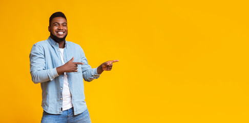 Cheerful black guy pointing two fingers aside at copy space