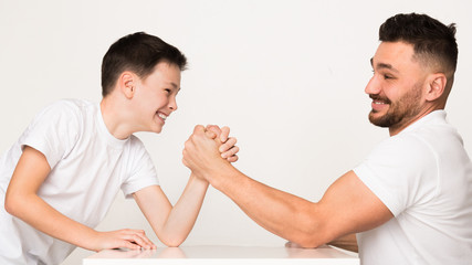 Fototapeta premium Playful dad and son compete in arm wrestling