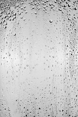 Drops of water flow down the surface of the clear glass on a gray background.