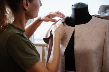 Skillful fashion designer stands in a dressmaker studio near the mannequin and fixes lace fabric on...