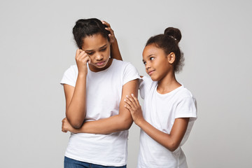 Little girl comforting her girlfriend over grey background
