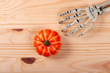 Halloween and decoration concept. Skeleton picking pumpkin over wooden background.