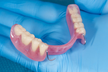 denture. Partial removable denture of the lower jaw of a person with white beautiful teeth in the hand of a dentist. Aesthetic Dentistry