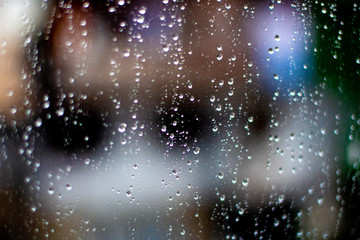 Naklejka na ściany i meble Drops of rain on glass. City in blur behind glass. Window splashed with raindrops. Misted glass.