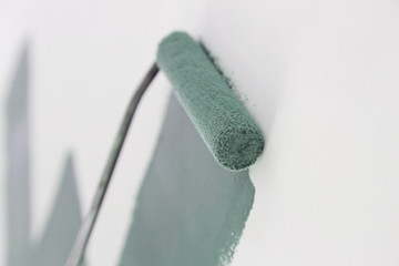 Paint roller. Process of painting with green paint over a white wall.	