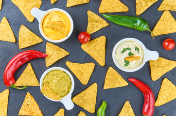 Nachos - yellow corn chips with various sauces in bowls: guacamole, cheese sauce, white sauce, on a dark background. Mexican food concept. The view from the top.