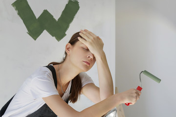 Tired exhausted young woman having problem with painting wall in her apartment, DIY home improvement difficulties	