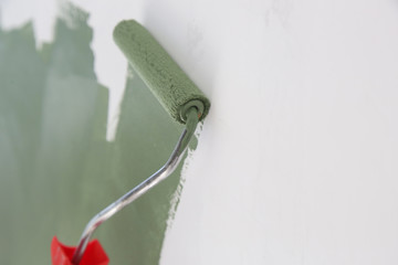 Paint roller. Process of painting with green paint over a white wall.	