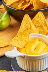 Nachos - yellow corn chips with various sauces in bowls: guacamole, cheese sauce, white sauce, on dark background. Mexican food concept.