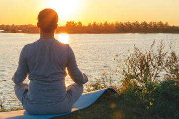 A young man sits on a lake at sunset, doing yoga. Sits in the pose of ardhapadmasana, padmasana. Balance, harmony, balance, concentration, relaxation.