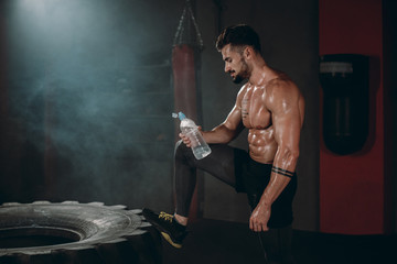 Details abs body athletic guy holding a bottle of water in a cross fitness class he wants to drink...