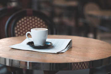 Cup of fresh organic coffee staying on open magazine on wooden table closeup. Breakfast time. Good morning.