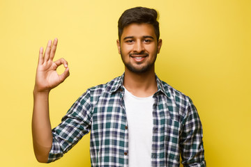 Young indian male looking like a tourist, okay sign concxept, isolated on yellow background.