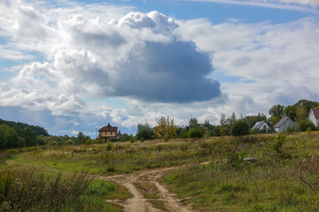 Fototapeta na wymiar Russian rural landscape in the fall, village houses near the forest. Sky with rain clouds