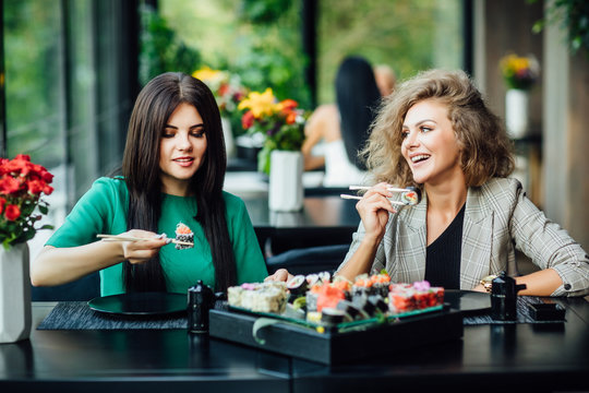 Two young girls sit in restaurant on the summer terrace and spend funny time with plate philadelphia.