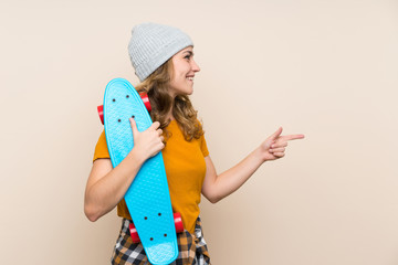 Young skater blonde girl over isolated background pointing to the side to present a product