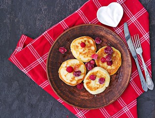 Cheesecakes with sour cream and frozen raspberries on a brown plate on a dark concrete background. Breakfast for Valentine's day concept. Cottage cheese recipes.