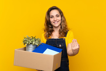Young blonde girl making a move while picking up a box full of things inviting to come with hand....