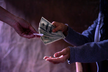 Woman hand with dollar banknotes buying drugs from a drug dealer, buying a dose of cocaine or...
