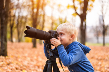 Little blond boy takes pictures on a SLR camera. Autumn Park